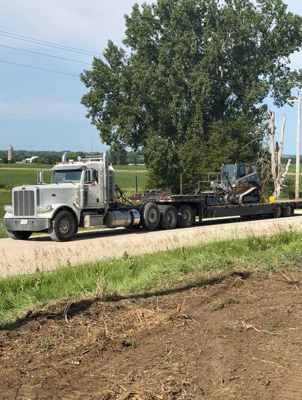 Precision Land Clearing truck hauling a John Deere skid steer