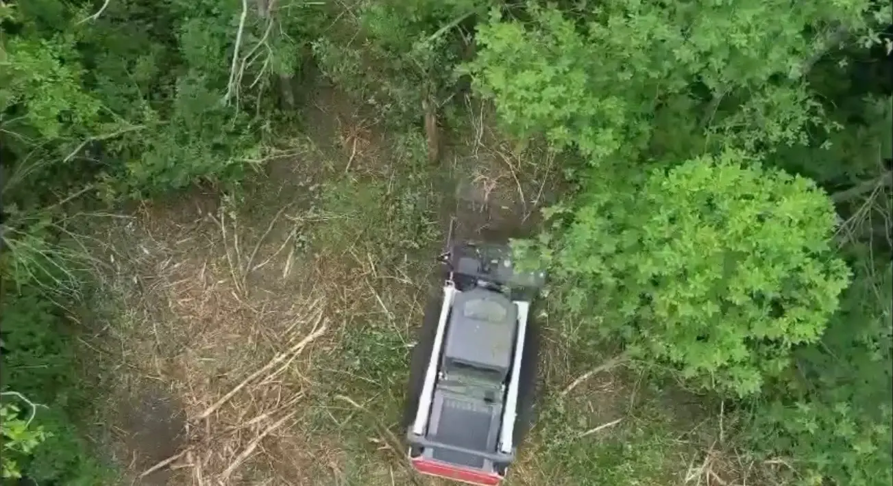 Aerial view of tracked equipment clearing vegetation among green trees