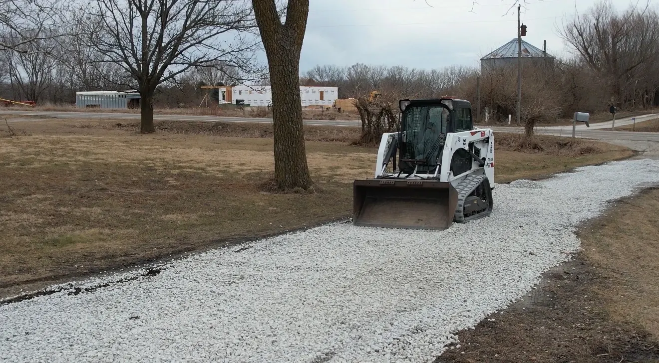 Skid steer spreading fresh gravel on a curved driveway