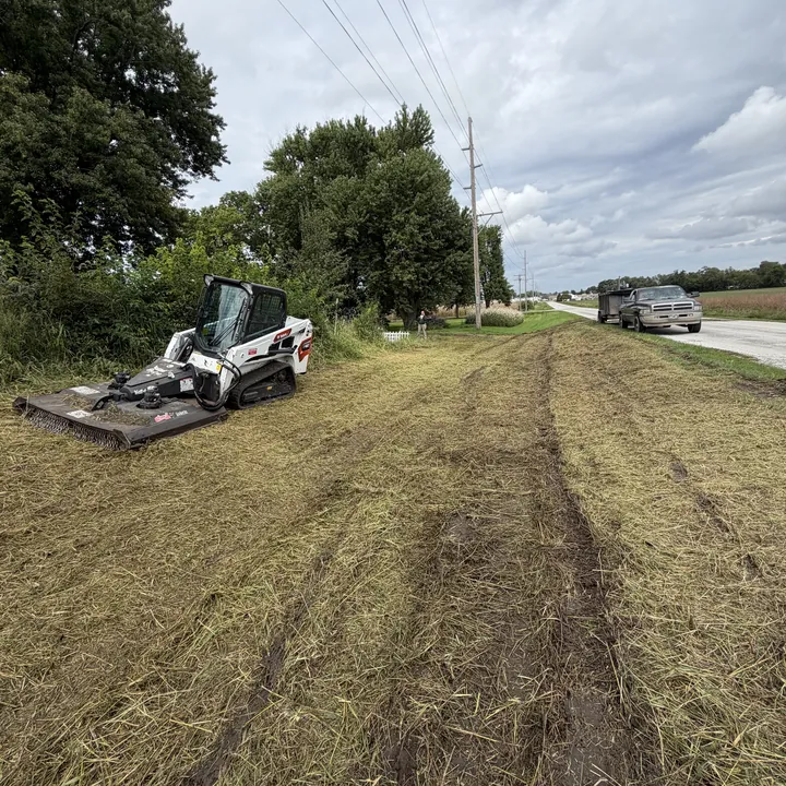 Skid steer mowing a strip along a country road